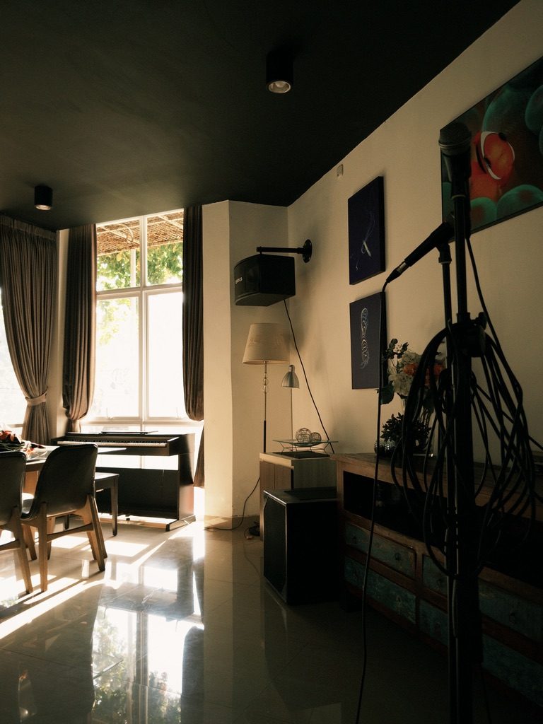 A recording room with a microphone stand, artwork on the walls and light through tall windows