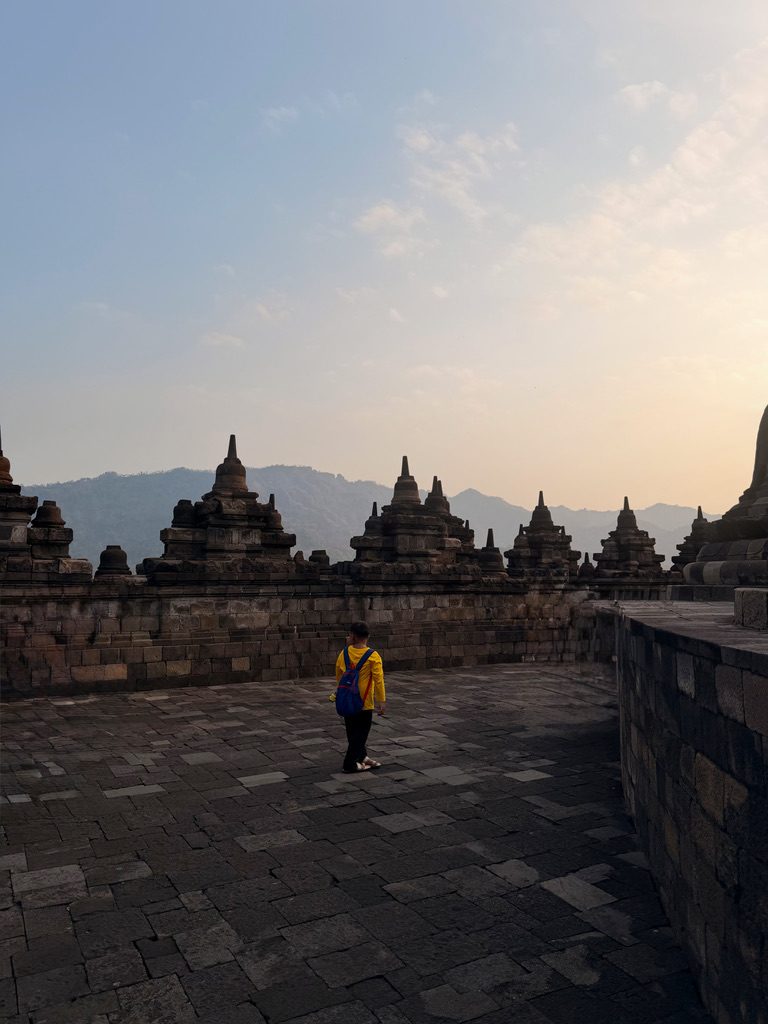 A visitor in a yellow jacket at Borobudur temple at sunset