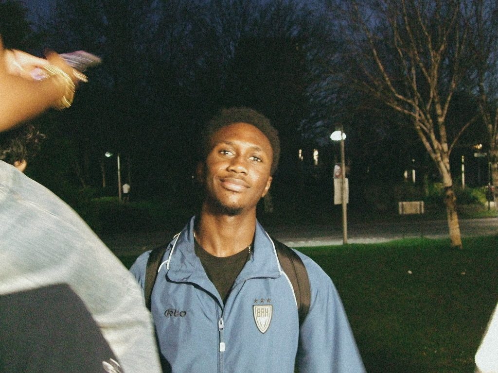 Kobi smiling, outdoors at night in a blue track jacket